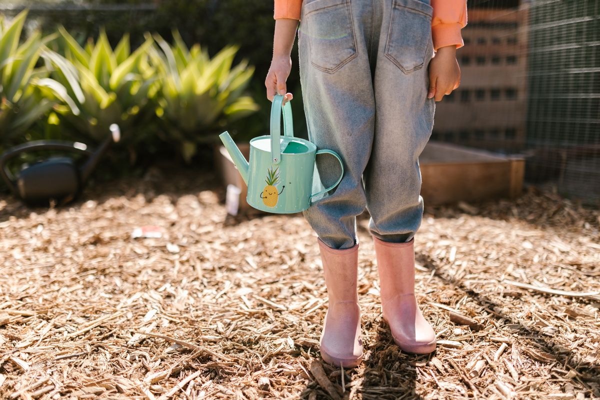 Kind mit Gießkanne und Gummistiefeln im Garten