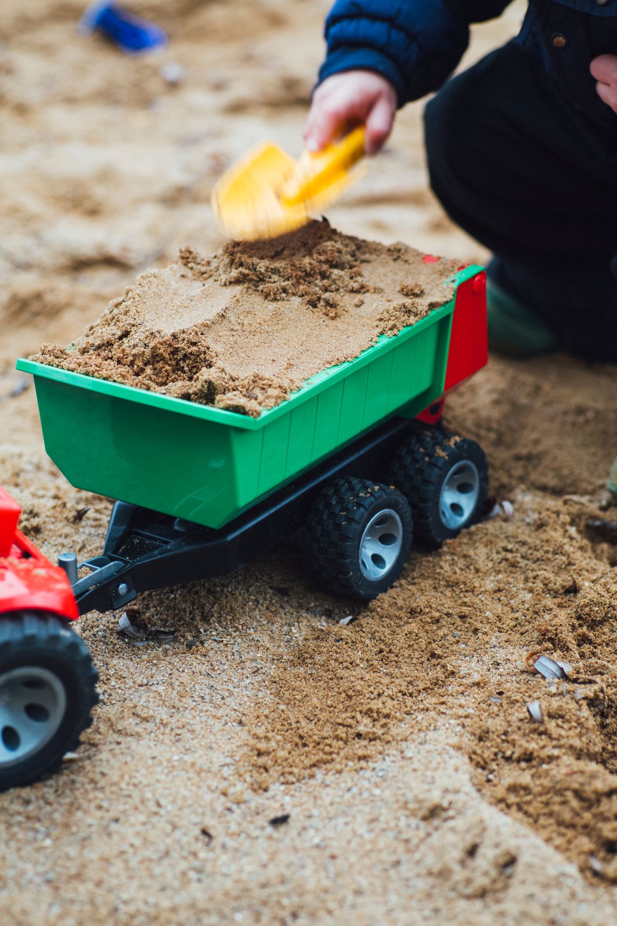 Kind schaufelt Spielsand in einen Spielzeug-Kipper im Sandkasten