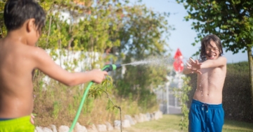 Zwei Kinder spielen im Garten fröhlich mit dem Gartenschlauch