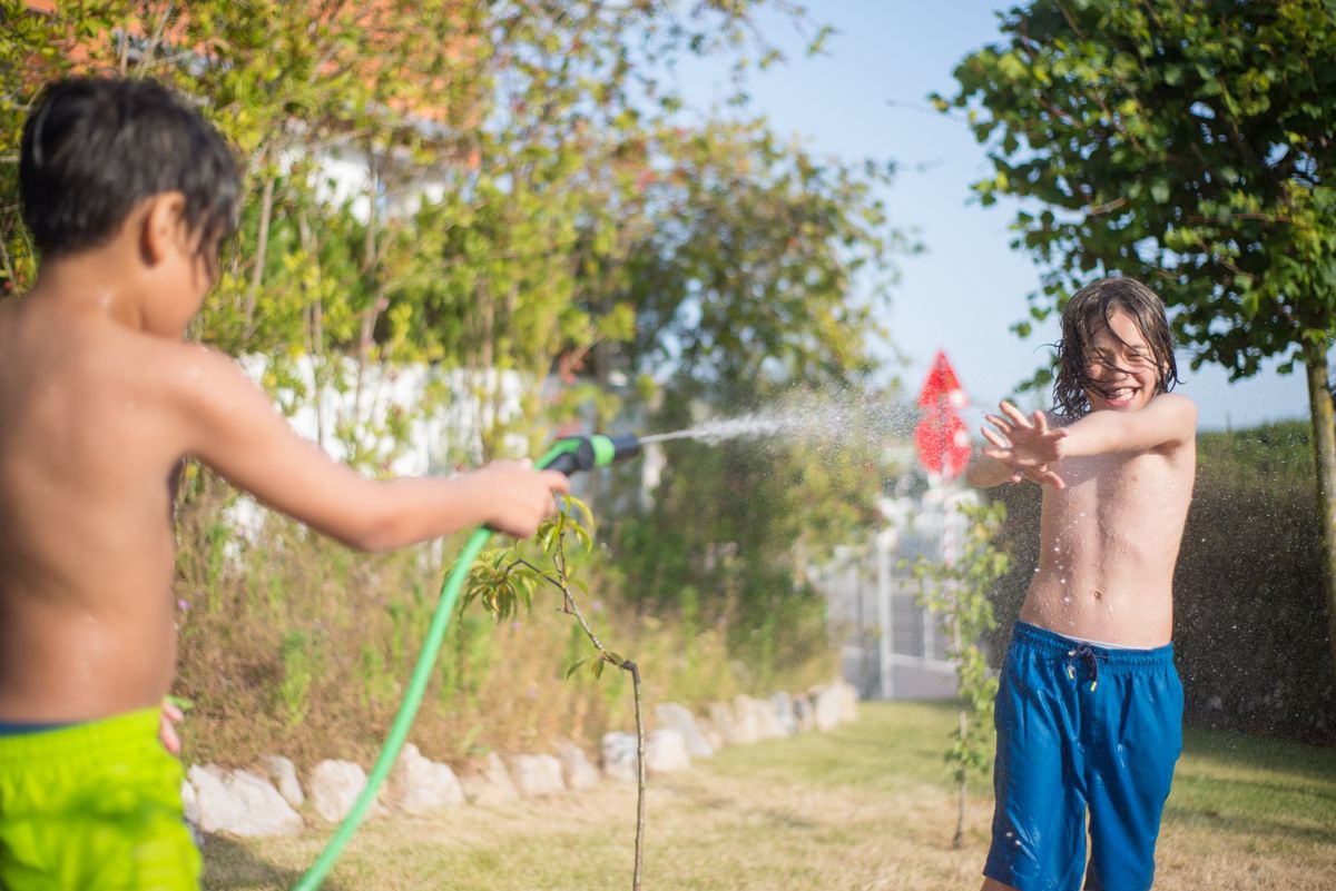 Zwei Kinder spielen im Garten fröhlich mit dem Gartenschlauch