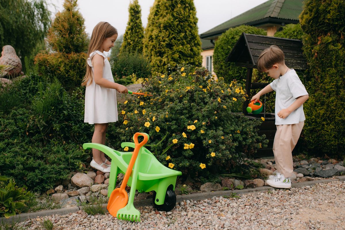 Zwei Kinder spielen mit Gartenwerkzeug im sommerlichen Garten
